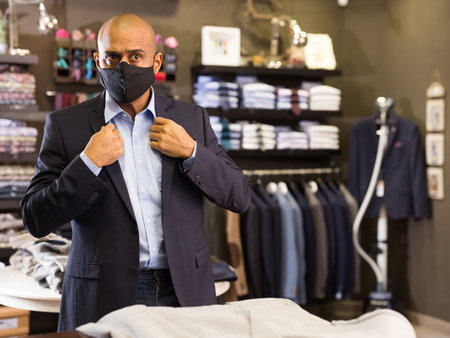 Man in mask choosing jacket in storeの写真素材