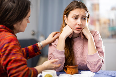 Woman comforting her friend while sitting at table with cups of teaの写真素材