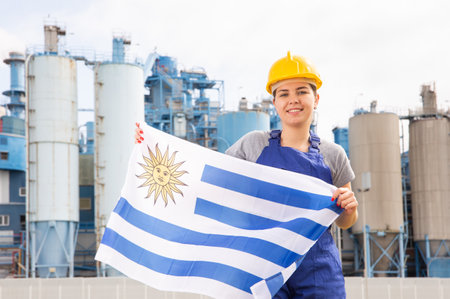 Happy woman waving flag of Uruguay against the background of modern factoryの写真素材