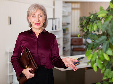 Positive friendly aged business woman inviting to officeの写真素材