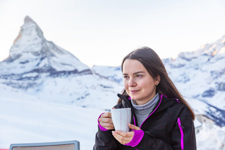 Dreamy woman enjoying mulled wine on background of snow covered mountainの写真素材