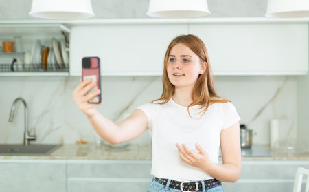 In kitchen holding smart phone in hand shooting selfie on front cameraの写真素材