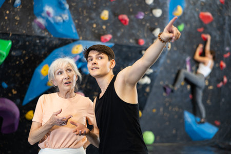 coach shows beginner female athlete simple routes for climbing on artificial dark bouldering wallの写真素材