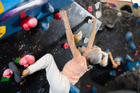 Mature female fitness climber training at bouldering gym.Woman rise up on artificial climbing wallの写真素材