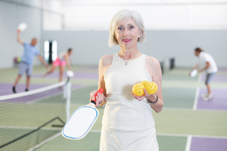 Smiling sporty elderly woman standing in indoor pickleball courtの写真素材