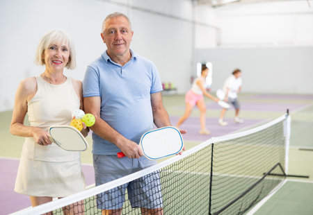 Elderly couple with rackets and balls posing on pickleball courtの写真素材