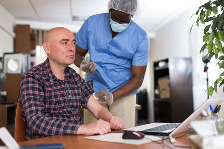 Entrepreneur getting vaccinated by african american doctor in officeの写真素材