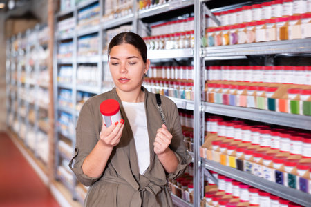 Young woman chooses bottles of paint in shopの写真素材