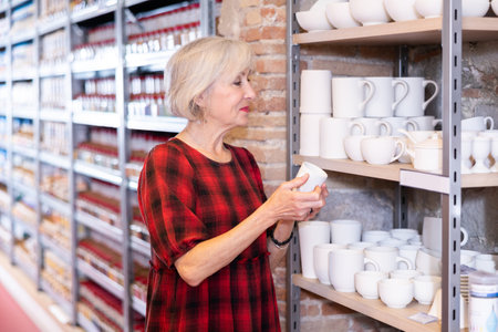 Elderly woman chooses mug or cup in pottery and ceramics shopの写真素材