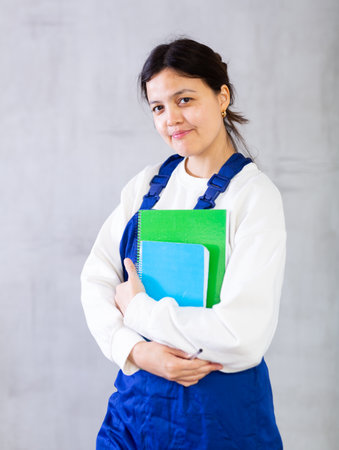 Young female mechanic in blue overalls holding workbooksの写真素材
