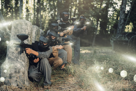 Group of paintball players aiming and shooting with guns outdoors
