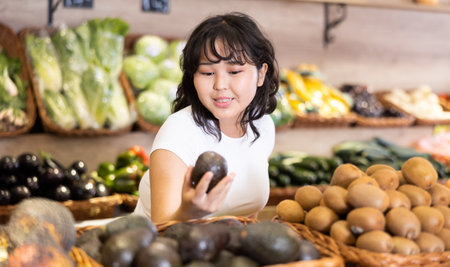 Pleased young woman purchaser choosing avocados in grocery storeの写真素材