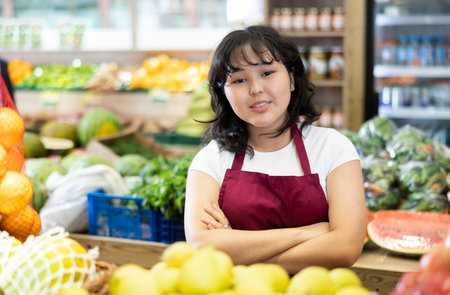Young saleswoman standing in front of counter in grocery storeの写真素材