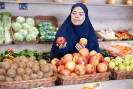 Girl in paranja making purchases in supermarket, choosing fresh applesの写真素材