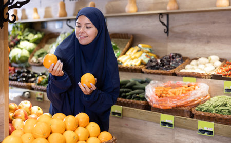 Delighted young Muslim woman purchaser choosing oranges in grocery storeの写真素材
