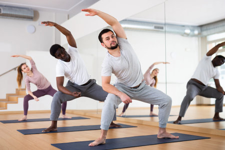 Young bearded man stretching during group yoga class