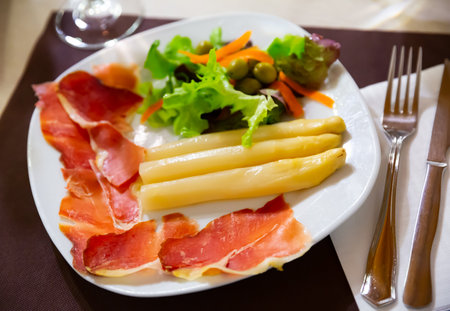 Slices of jamon with asparagus, lettuce and carrot on tableの写真素材