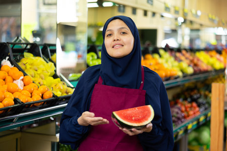 Positive woman seller in hijab holds in her hands half of ripe thin-crusted watermelonの写真素材