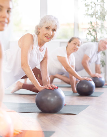 Group of mature active people doing soft ball exercises during group pilates class in fitness studioの写真素材