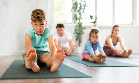 Diligent preteen boy sitting on the floor and practicing stretching with his familyの写真素材