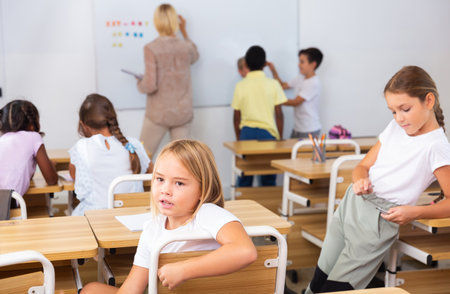 Positive primary school students are talking about homework at deskの写真素材