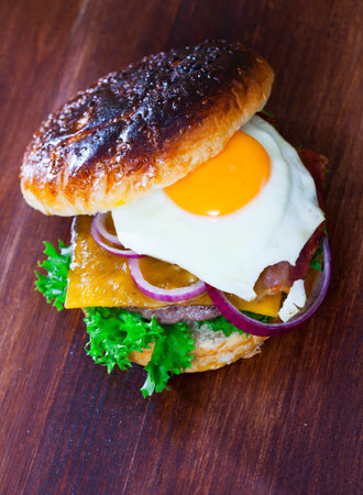 Burger with fried egg, bacon, cheese, onion and lettuceの写真素材