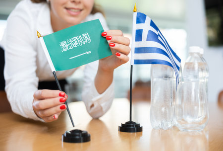 Unrecognizable girl sets midget flags of Greece and Saudi Arabia before international negotiationsの写真素材