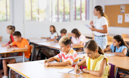 Boys an girls sitting at lesson in classroom, teacher standingの写真素材