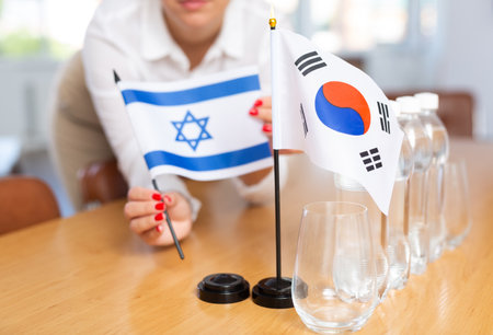 Female hands placing flags of South Korea and Israel on negotiating tableの写真素材