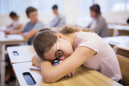 Exhausted teen girl sleeping at desk during lessonの写真素材