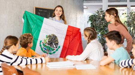 Young female teacher showing flag of Mexico to schoolchildren preteens during history lesson in classroomの写真素材