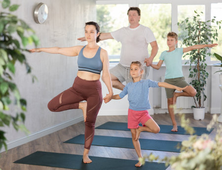 Mom and dougter keep balance standing in Vrikshasana on one leg and holding each other s handの写真素材