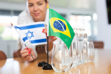 Female secretary places flags of the Israel and Brazil flag on table before the negotiations of top political figuresの写真素材