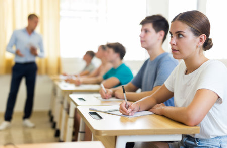 Teenage girl student listening to lecturer and writing in workbookの写真素材