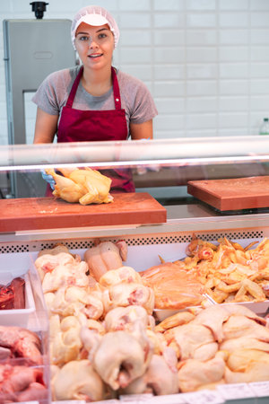 Young saleswoman laying raw broiler chickens in display caseの写真素材