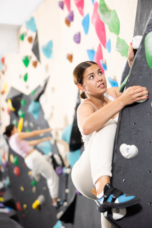 Young female alpinist practicing indoor a rock-climbing on a artificial boulder without safety beltsの写真素材