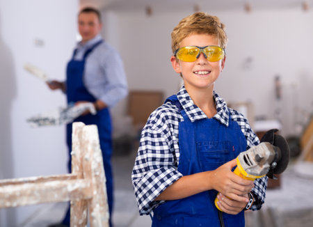 Portrait of little boy in protective glasses with an angle grinder in his hands in room being renovatedの写真素材