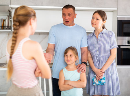Disgruntled parents reprimanding eldest teenage girl in home kitchenの写真素材