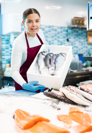 Female seller in apron shows hands fish dorado on counter in supermarketの写真素材