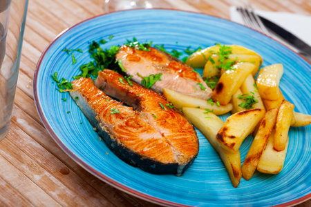 Roasted salmon steaks with fried potatoes and greensの写真素材