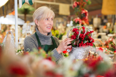 Aged female seller placing Christmas decorations on showcaseの写真素材