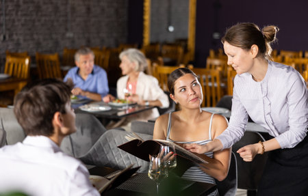 Waitress helps to sort out menu, choose original dish to young married coupleの写真素材