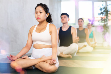 Young woman practicing lotus pose of yoga in light fitness roomの写真素材