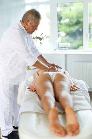 Skilled old masseur conducting back massage for woman clientの写真素材