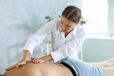 Skilled middle-aged masseuse conducting back massage for man clientの写真素材