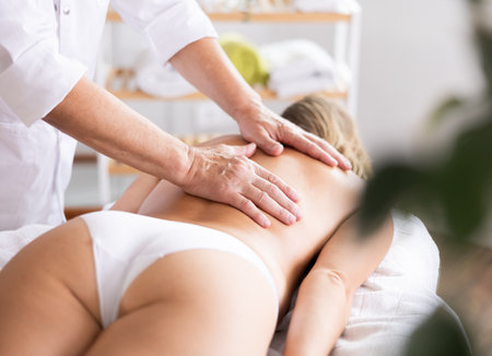 Hands of old masseur conducting back massage for woman clientの写真素材