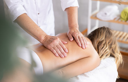 Hands of old masseur conducting back massage for woman clientの写真素材