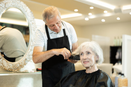 Experienced hairdresser using round hairbrush to style hair to elderly womanの写真素材