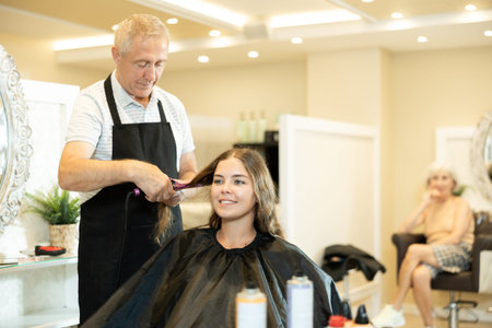 In beauty salon, elderly man makes styling curls for young girl client