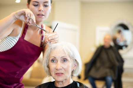 Young woman master completes creation of senior female clients image with help of scissorsの写真素材